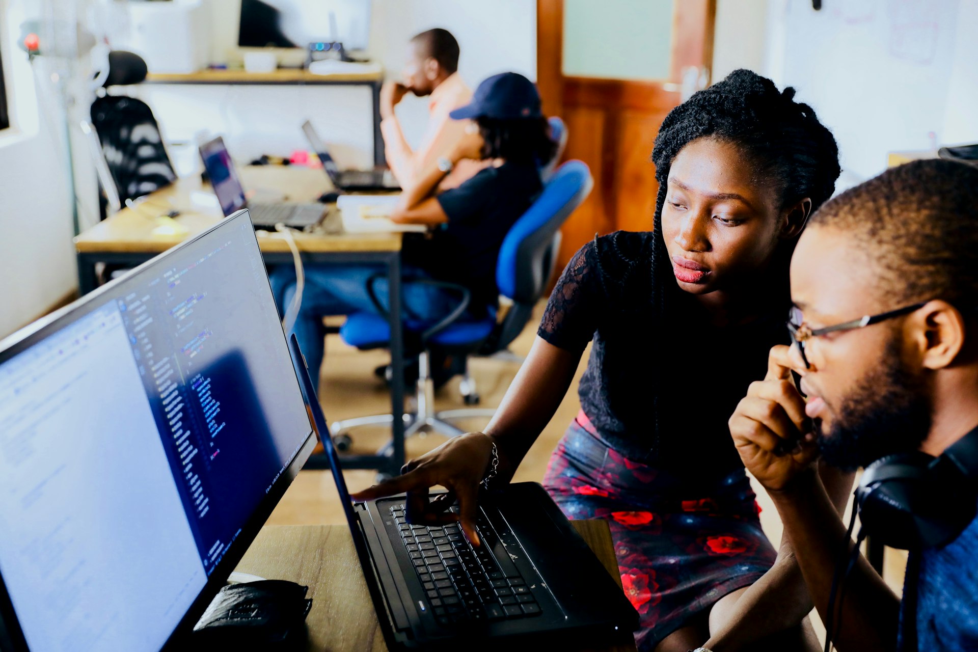 Two colleagues working through a problem together at a laptop in a busy office