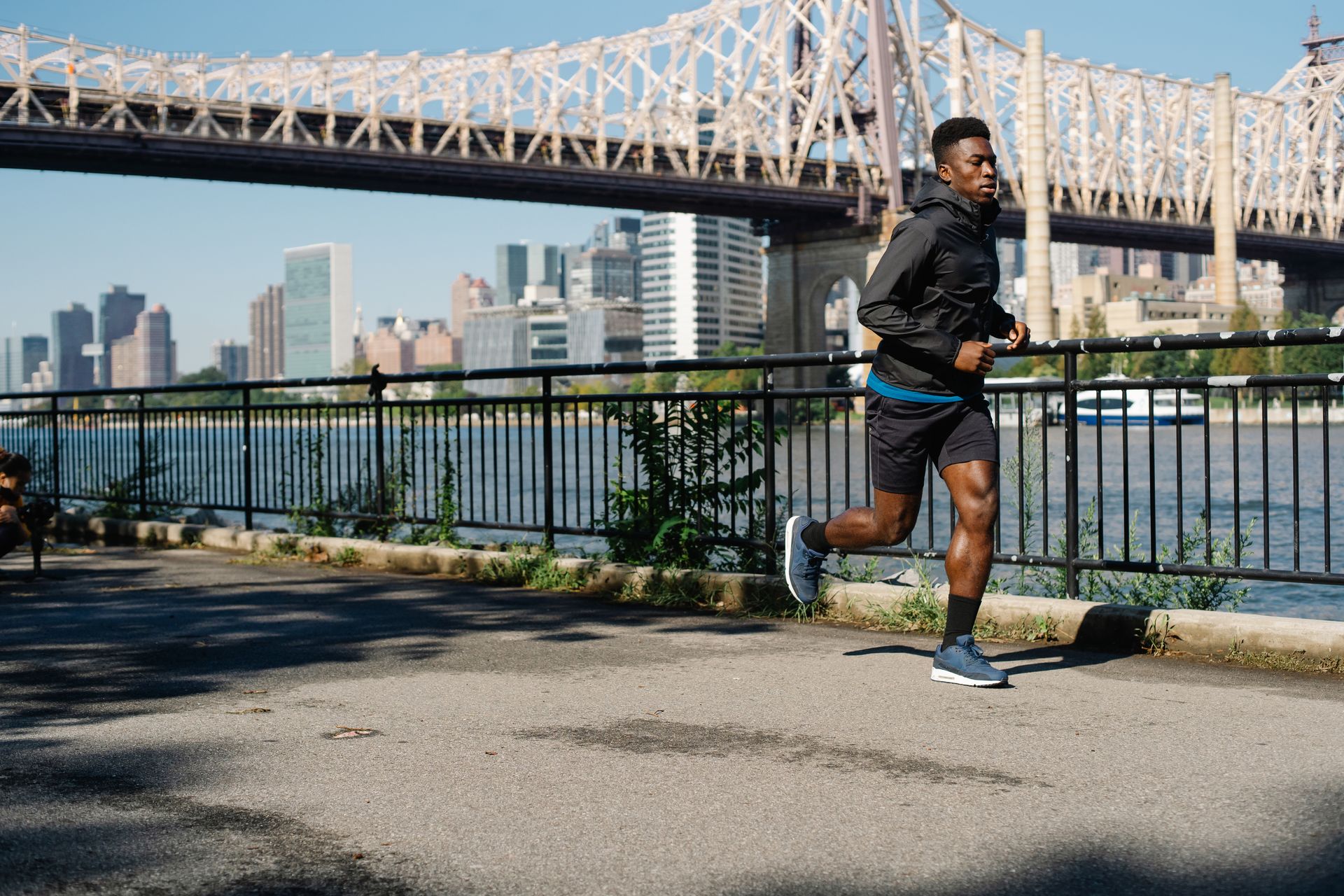 A man running alone along a riverside path with the city skyline behind him
